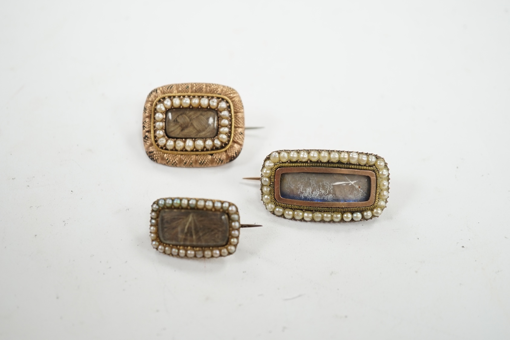 Three assorted 19th century yellow metal and seed pearl set mourning brooches, two with plaited hair beneath a glazed panel, largest 27mm. Condition - poor to fair